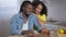 Positive handsome African American man closing laptop and talking with loving woman in kitchen at home. Portrait of