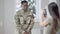 Positive handsome African American man in military uniform grimacing as Caucasian woman taking photos on smartphone