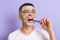 Positive happy man wearing white t shirt applying mask with cucumber slices on his face brushing his teeth, holding toothbrush in