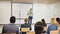 Positive Hispanic woman standing with microphone on stage in conference room, speaking to businesspeople at seminar