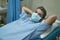 Positive and hopeful hospital patient recovering from covid-19 - young attractive and trustful man in mask lying on clinic bed