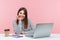 Positive inspired brunette woman sitting at laptop on her office and looking at camera with toothy smile, making notes and