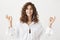 Positive joyful caucasian adult female with curly hair smiling and standing in meditating pose with zen gestures, being