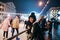 Positive lady in winter clothes stands at the rink at the Christmas street in evening and poses for the camera. Portrait of a cute