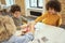 Positive little diverse boys laughing while sitting at the table and examining details of a robot during STEM class