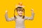 Positive little girl with funny pigtails shows her power biceps with arms raised victory, book and apple on head. Winner school