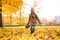 Positive little girl walking through the fallen leaves in autumn park on cheerful fall day