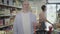 Positive male buyer posing with shopping basket in grocery as blurred woman choosing goods at the background. Portrait