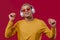 Positive man listening music, enjoying dance with headphones on red studio background. Radio, wireless modern sound