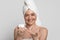 Positive mature woman with towel on head holding jar with moisturising cream