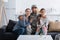 Positive men in camouflage uniform hugging family on couch near american flag at home,stock image