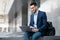 Positive middle eastern guy sitting on the street, using laptop