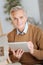 Positive minded elderly man enjoying working on tablet computer