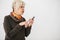 A positive modern elderly woman is holding a cell phone and is using it. The older generation and modern technology.