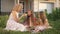 Positive mother and daughters eating delicious healthful peach and apple on picnic outdoors at sunset. Wide shot of