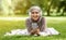 Positive muslim girl lying on blanket at park, using phone