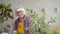 Positive older woman pensioner sprays home plants in her living room close up