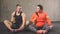 Positive overweight woman and fit guy doing exercises while sitting on the floor.