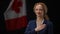 Positive politician woman holding hand on chest listening to national anthem. Smiling lady standing at black background