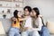 Positive pretty young japanese girl, mom and dad hugging on sofa have fun, enjoy tender moment