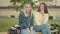 Positive redhead girl whispering on friend`s ear as sitting on bench on university yard. Joyful charming Caucasian