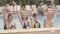 Positive relaxed Caucasian women dancing in water at poolside with blurred multiracial men sitting at the background