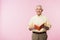 positive retired man holding book and smiling on pink.