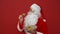 Positive Santa eats delicious chocolate chip cookies with plates on red wall background. Christmas concept