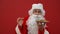 Positive Santa sniffs cookies from a plate and shows thumbs up on a red background. Christmas concept