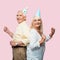 positive senior husband and wife in party caps gesturing isolated on pink.