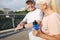 Positive senior man with smartwatch looks at blonde woman training together on footbridge