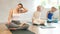 Positive senior woman practicing yoga during group class in fitness studio, sitting on mat and doing neck stretching in