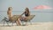 Positive slim young women rubbing sunscreen on tanned body on sandy beach. Portrait of confident young Caucasian