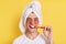 Positive smiling Caucasian man wrapped towel on head doing morning cosmetology procedures and brushing teeth, posing with patches
