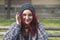 Positive smiling homeless red hair girl sitting on the bench on the street and looking in the camera while she having fun