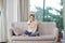 Positive smiling optimistic young woman sit indoors at home watch tv holding remote control on sofa