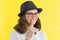 Positive smiling teenage girl 13.14 years old with glasses, a hat shows a sign of silence, holds a finger on her lips, a yellow st