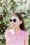 A positive smiling young girl in sunglasses poses against a blooming Apple tree in warm weather Selective focus