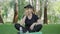 Positive sportive woman smelling and biting apple as sitting on exercise mat in summer park. Portrait of confident