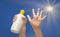 Positive symbol drawing by sunscreen on open hand. Another hand holding a bottle of sun cream. Blue sky, beams of sun background.