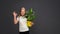 Positive teen girl shows ok gesture holding houseplant, green flower in yellow pot. Isolated on gray background. Copy