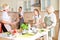 Positive teen girl washes the dishes while others prepare food at table