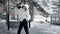 Positive teenager girl in white hat and jacket dancing outdoor on snowy street in winter park. Happy young woman dancer