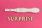 A positive test for pregnancy and the word `surprise` made of wooden letters on a pink background