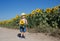 Positive toddler boy in yellow hat and shorts with a sunflower in his hands is standing on a field of sunflowers