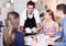 positive waiter bringing ordered dishes to friends in tearoom
