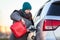 Positive woman driver pouring petrol from red plastic gasoline can into a car tank