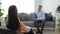 Positive woman psychologist talking to patient sitting on chair in clinic office