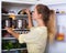 Positive woman searching products on refrigerator