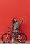 Positive woman sitting on a bicycle on a background of a red wall and taking a selfie on a smartphone. . Vertical